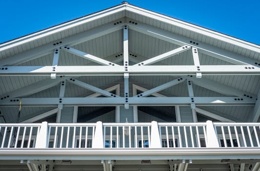Low-angle view of a modern white house exterior showcasing wooden trusses and a clear blue sky.